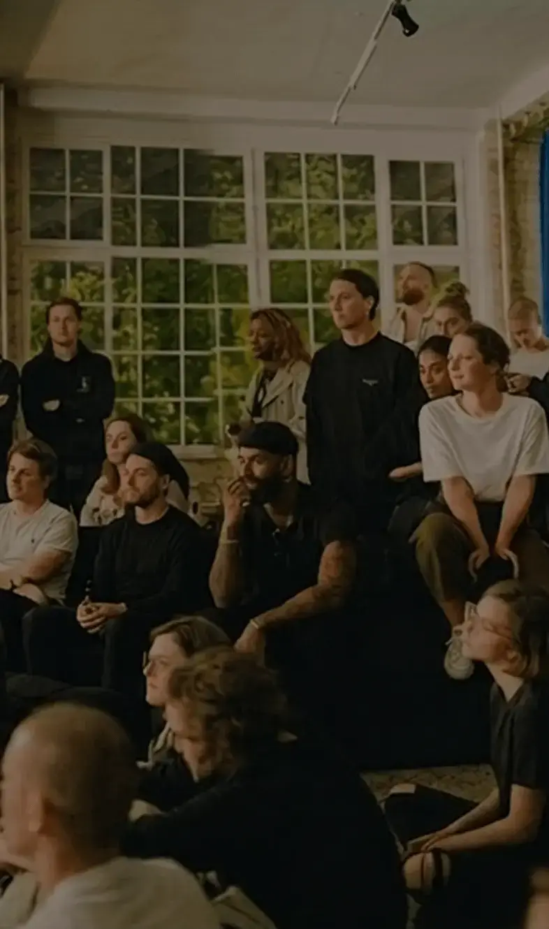 A group of people sitting and standing together in a bright room, watching something off-camera